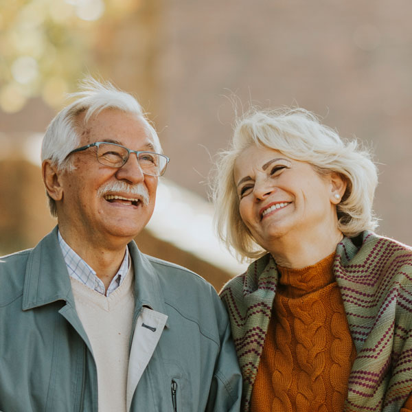 Older couple smiling and walking through a park
