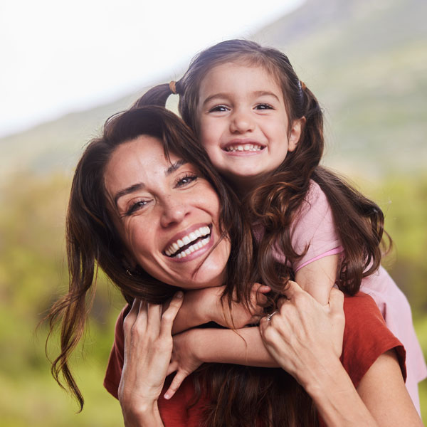 Happy mom carrying her smiling daughter on her back